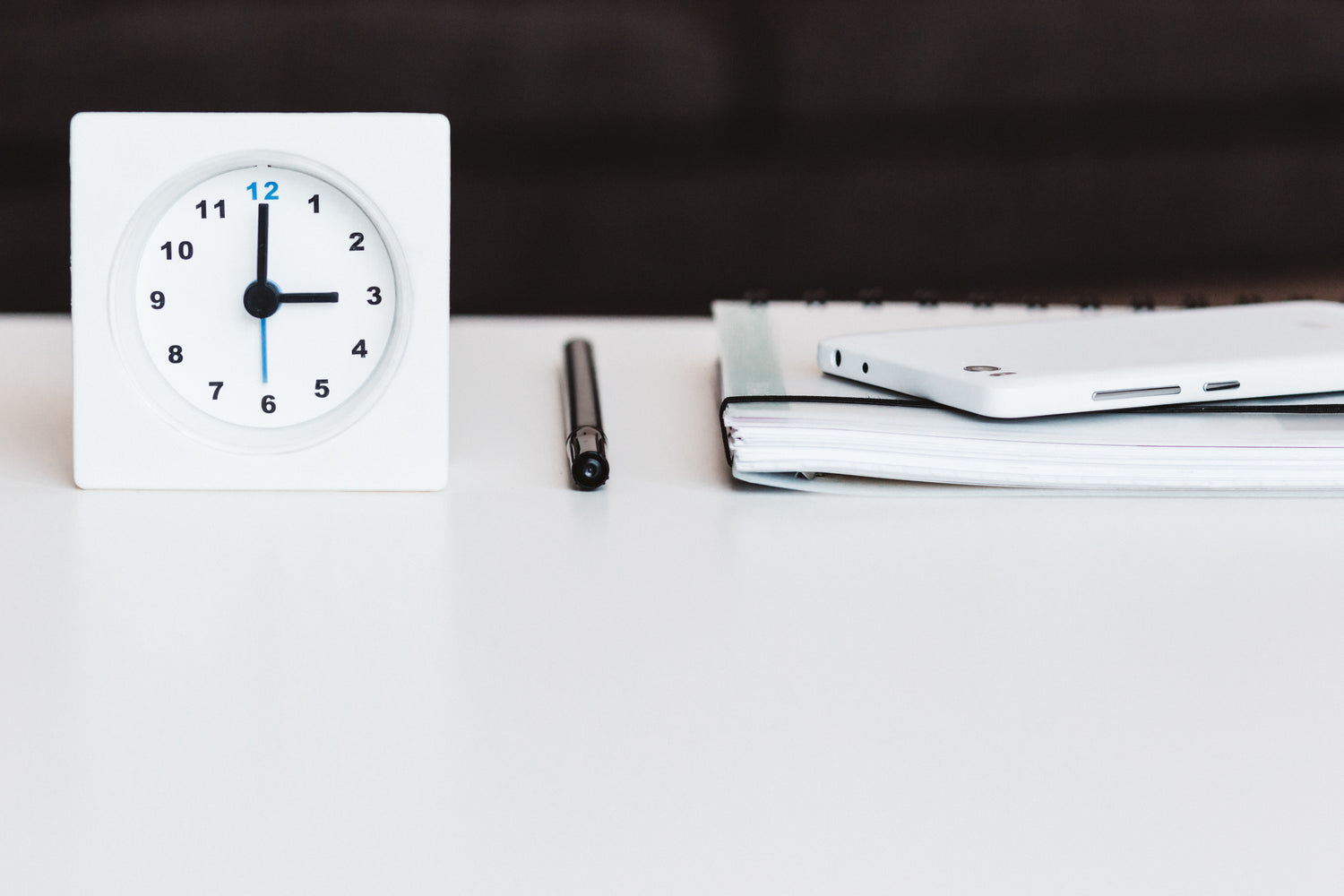 a clock on a desk, a notebook, and a pen